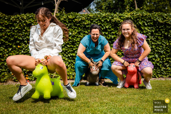 At an outdoor reception venue, the jovial wedding guests were competitively jumping and bouncing on the grass with the children's toys Outdoors at a Noord Brabant reception venue, wedding guests are playing with jumping bouncing kid toys on the grass