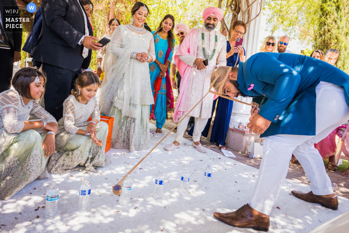 The funny actions of a groomsman providing a source of joy and amusement to the newlyweds and their families is a cherished memory from their wedding day From the Lake Oak Meadows Weddings and Events in Temecula, California, image of a groomsman playing a game with the groom and the bride's family after the wedding ceremony