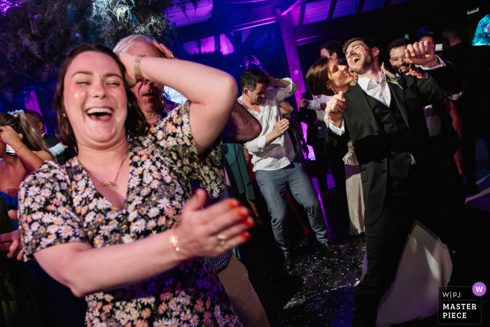 Inmitten der fröhlichen Feierlichkeiten ist das Brautpaar im Hintergrund des Fotos zu sehen, wie es sich anmutig wiegt, während ein fröhlicher Gast im Vordergrund tanzt Bei der festlichen Empfangsparty im Alto da Capela in Porto Alegre tanzen RS-Brautpaare im Hintergrund, während ein Gast im Vordergrund tanzt