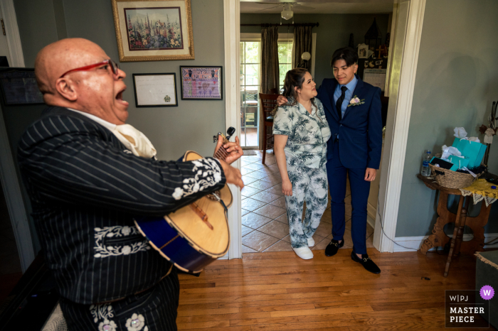 Bild aus einem Haus in Lenoir City, Tennessee, das ein Mariachi-Bandmitglied zeigt, das im Wohnzimmer der Braut aus vollem Halse singt, während sie mit ihrem Bruder zuschaut