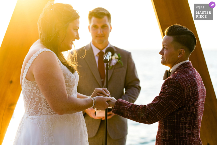 A couple exchanges wedding rings at The Arch in South Lake Tahoe, California. They stand against a beautiful sunset backdrop.