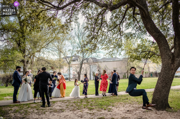 HOUSTON, TEXAS - Guests gather at the reception in Houston, Texas, for a pre-ceremony moment as a male guest rides on the tree swing.