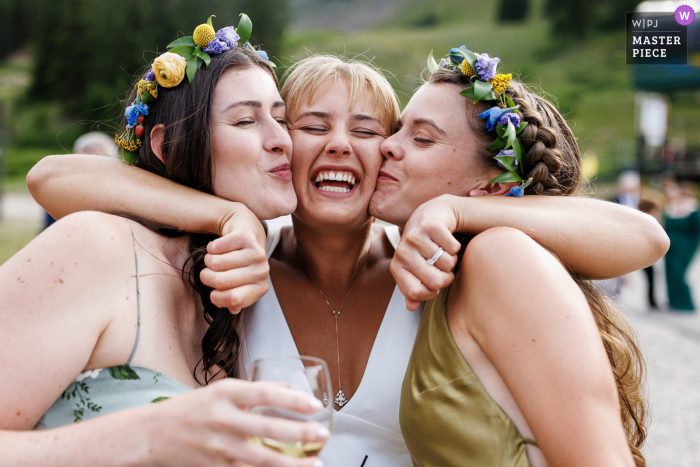 Bride's Heartfelt Bonding: A Captivating Cocktail Moment at Black Mountain Lodge The bride shares heartfelt hugs and kisses with two girlfriends during the cocktail hour at Black Mountain Lodge in Arapahoe Basin, Colorado.