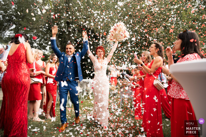 Newlyweds Embrace in Love and Laughter at Théâtre du Moulinage in France with Matchy Guests in Red Excitement and love filled the air as the newlyweds embraced on the steps of Théâtre du Moulinage in France, surrounded by their guests in matching red attire.