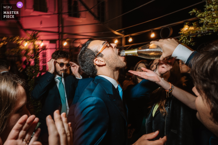 The groom takes a sip from the bottle, as his friend pours more into his mouth, at the Matrimonio Villa Ala wedding in Rivalba, Italy.