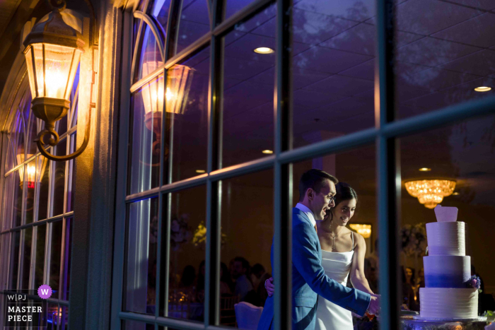 Love and light intertwine as the newlyweds share a special moment cutting their cake, captured beautifully against the dusk view of a New Jersey sky.