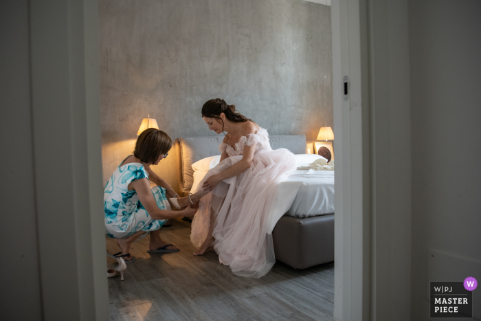 In Florence, the bride prepares for her special day, receiving a helping hand with her shoes in the comfort of her hotel room.
