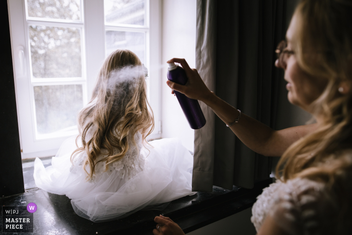 Mother Spruces Up Daughter's Hair While Waiting on Guests in Hohe Bracht, Germany Preparing for the big day, a mother helps her daughter's hair with a touch of hairspray, while keeping an eye on the arriving guests in scenic Hohe Bracht Germany.