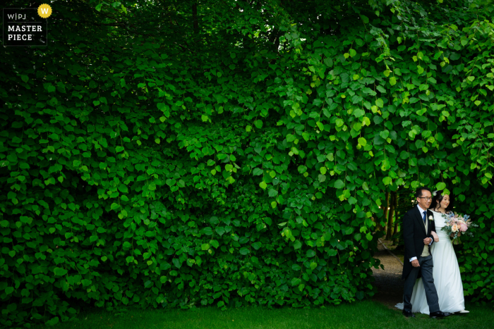 The Bride's Walk With Dad at Langshott Manor in England | A Fairytale Moment Among the Pretty Green Scenery Amidst a sea of lush greenery, the bride is escorted down the aisle by her father at the picturesque Langshott Manor in the UK.