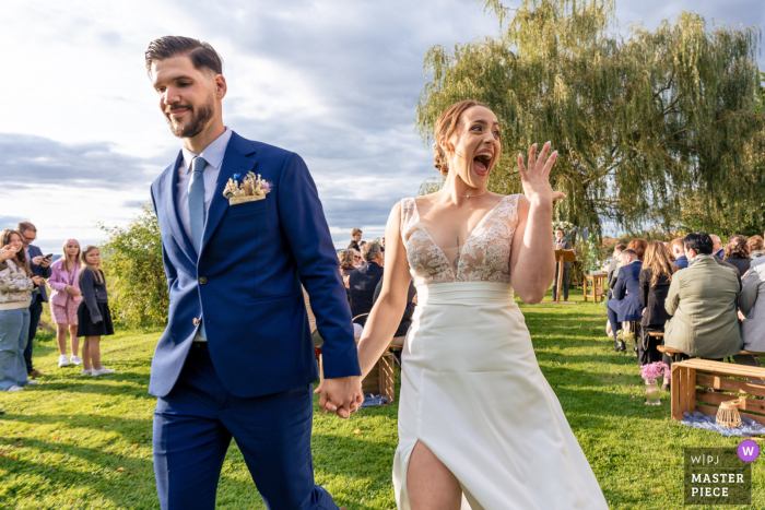 Beaming Bride Leaves French Wedding Showing Ring at Seicheprey Chateau Filled with pure happiness, the newlywed bride radiates pure joy as she walks out of the beautiful outdoor ceremony at the enchanting Petit chateau de Seicheprey in France.