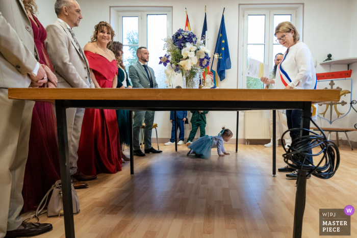 Cute Kid Crashes Legal Marriage Ceremony in France Amidst the solemnity, an adorable toddler takes center stage in this image, crawling under the official table at the legal ceremony in Cons la Granville, France.