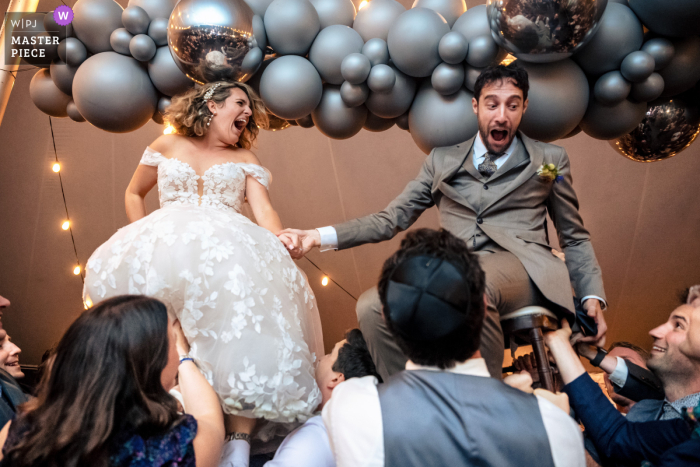 The Wedding Party: SoCal Guests Lift Bride & Groom During Horah under Balloon Decorations At their Southern California wedding, the bride and groom's guests added some playful fun to the reception's horah by lifting them up under beautiful balloon decorations.