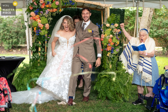 Rabbi Watches as Newlyweds Happily Break Glass in Sunny SoCal Ceremony! In sunny Southern California, the bride and groom joyfully smash the glass under the supervision of their rabbi, marking the end of their outdoor ceremony.