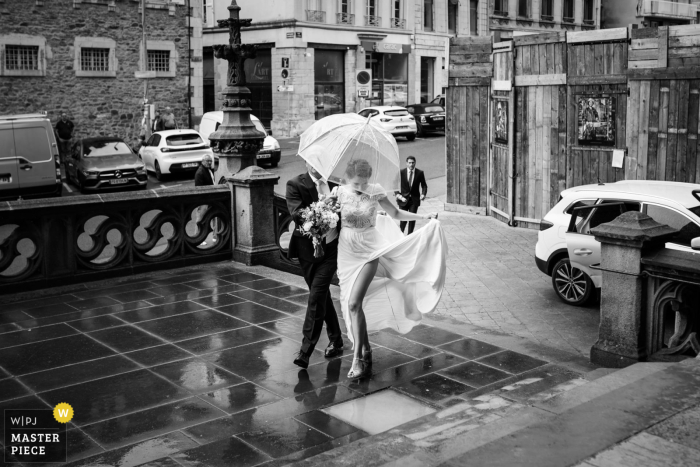 Beautiful Bride Shines in Timeless Elegance Outside a Toulouse Church, in Romantic Rainfall, in Stunning Black and White A radiant bride, adorned in timeless elegance, gracefully makes her grand entrance at a Toulouse church, under a romantic rainfall, captured in stunning black and white.