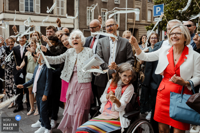 Guests Celebrate Newlyweds in Angers, France: Smiles, Ribbons, and Excitement! As they exit the church, the guests hold up ribbons with smiles and excitement, ready to welcome and congratulate the newly married couple in Angers, France.
