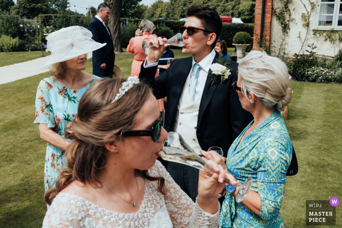 Staffordshire Sweethearts Sip Champagne, Sharing a Moment in a Beautiful Garden Wedding Amidst the beauty of her Staffordshire garden, the bride and groom share a special moment, toasting Champagne to their new life together.