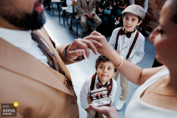 The newlyweds' commitment is witnessed by their children during the heartwarming exchange of rings, captured by a WPJA photographer at La Factory Thizy les bourgs.
