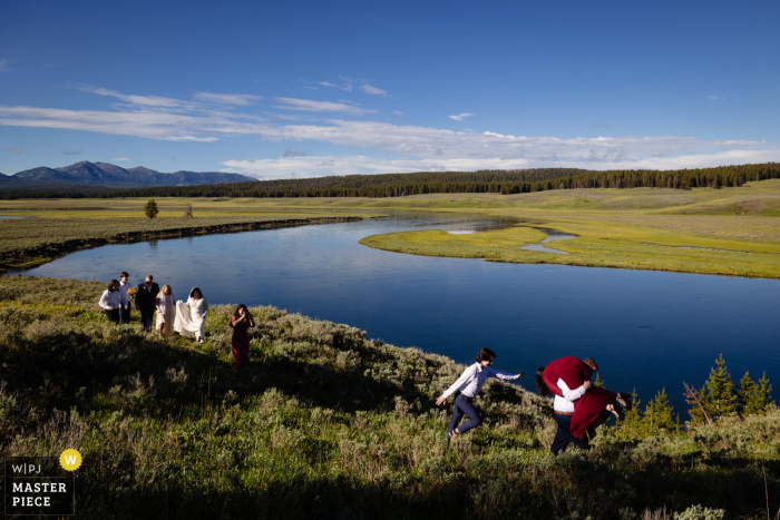Helping a Lady in Heels in Yellowstone: A Wild Wedding Adventure through the Mud near the Water Amidst the wild and breathtaking landscape of Yellowstone, a guest braves the muddy terrain to help a girl in heels navigate her way by the water.