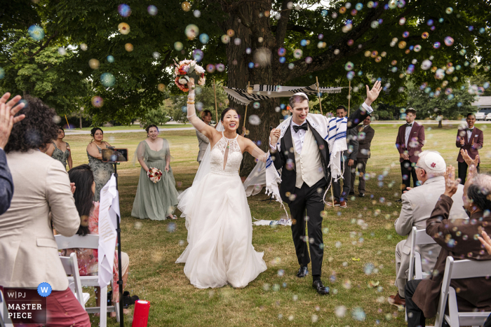 Hand in hand, the newlyweds exit the aisle, surrounded by a whimsical bubble-filled celebration at Endicott Estate in Dedham, MA.