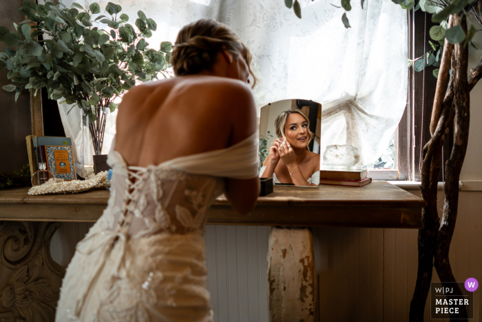 With grace and poise, the bride prepares for her special day putting on her jewelry in the bridal suite mirror, at Twin Oaks Wedding Venue in San Marcos, CA.