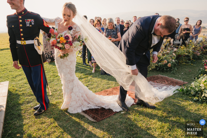 Captured by a WPJA photographer at Sage Lodge, this hilarious moment shows the brother of the bride tripping over his sister's veil and wedding dress after walking her down the aisle at a Montana wedding.
