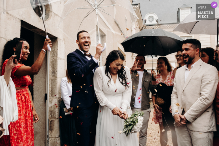 Newlyweds Emerge from Chateauroux City Hall in Joyful Rain and Confetti on Their Wedding Day The newlyweds emerge from the Mairie de Chateauroux, surrounded by a shower of rain and confetti, capturing the joy of their special day.