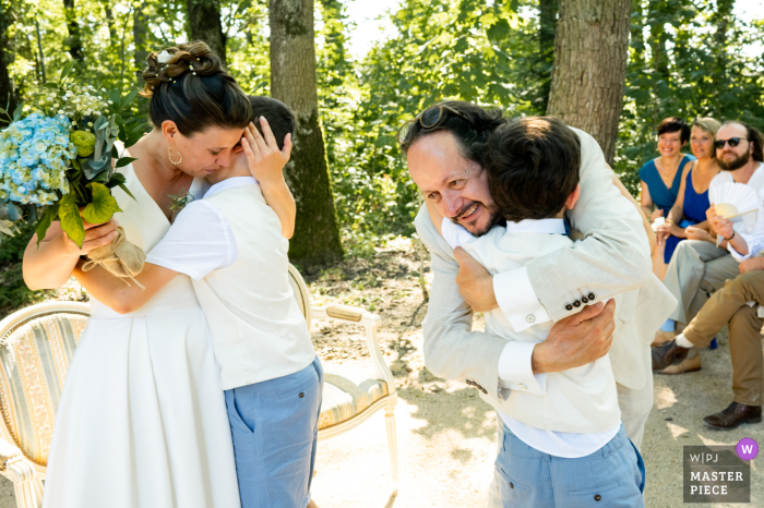 Lovely Family Hugs at Domaine du Clos des Liesses in a Serene Wedding Setting A heartwarming family moment as the couple embraces the little ones amidst the serene backdrop of Domaine du Clos des Liesses during the wedding ceremony.