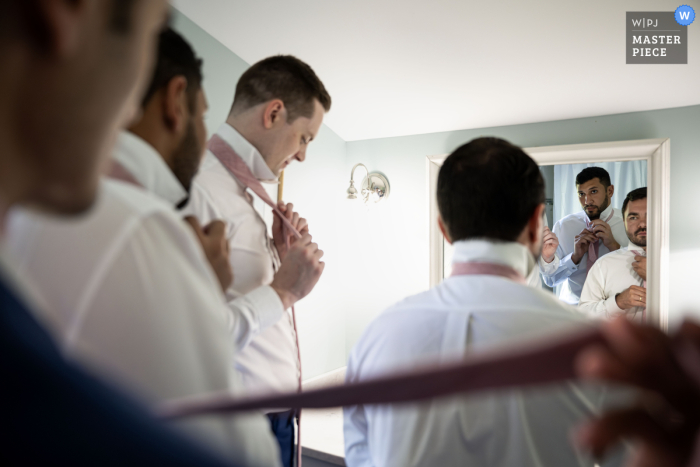 Amid the chaos of wedding preparations, the groom and his groomsmen squeeze into a cramped bathroom to perfect their ties before the ceremony at a private residence in Westerly, RI.
