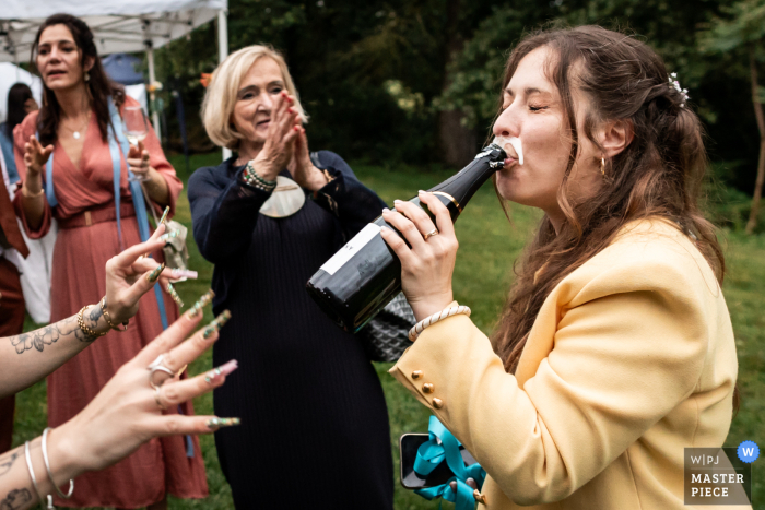 Surrounded by the beautiful scenery of Les Tables de Crespin in Tarn, France, the bride's friend enjoys champagne straight from the bottle during the lively reception.