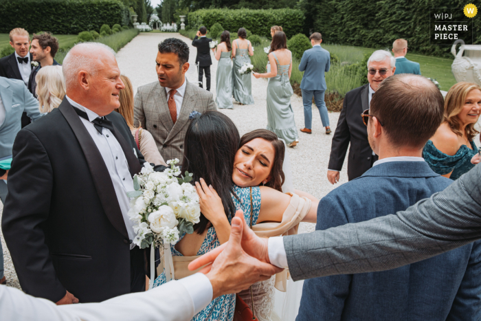 Bride Shares Affectionate Embrace While Guest Exchanges Handshake at Chateau La Durantie Gathering In the picturesque setting of Chateau La Durantie, the bride embraces a guest with affection, as another guest engages in a friendly handshake nearby, highlighting the warmth and connection of the gathering.