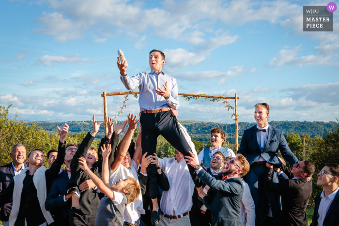 Guest Catches Sausage Tossed by Groom Amid Laughter at Domaine des Plagnes, Saint-Hilaire-de-Brens, France At Domaine des Plagnes in Saint-Hilaire-de-Brens, France, laughter fills the air as a guest skillfully catches a sausage tossed by the groom, adding a playful twist to the celebration.