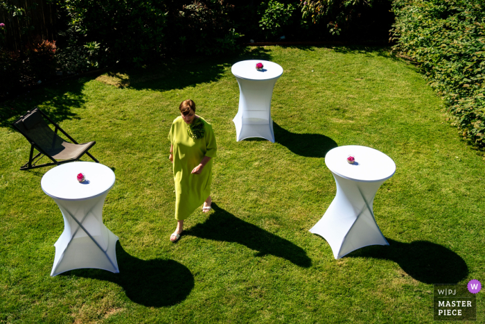Mother's Shadow Mimics Bar Tables in Whimsical Sunlit Scene on Grass As the mother walks gracefully across the grass, her shadow mimics the tall, slender shapes of the nearby bar tables, creating a whimsical image in the sunlight.