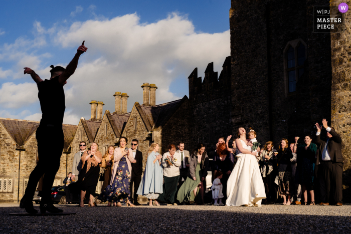 Irish Dancer Captivates Crowd in Radiant Sunlight at Kilkea Castle In the enchanting setting of Kilkea Castle, an Irish dancer enchants the crowd, skillfully moving in the shadows, with the radiant sunlight casting an ethereal glow on the guests.