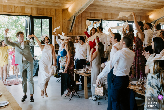 In Normandy, France, the bride and groom make a spirited entrance to their dinner, both caught mid-air as they hop with joy, capturing a lively and joyous moment.