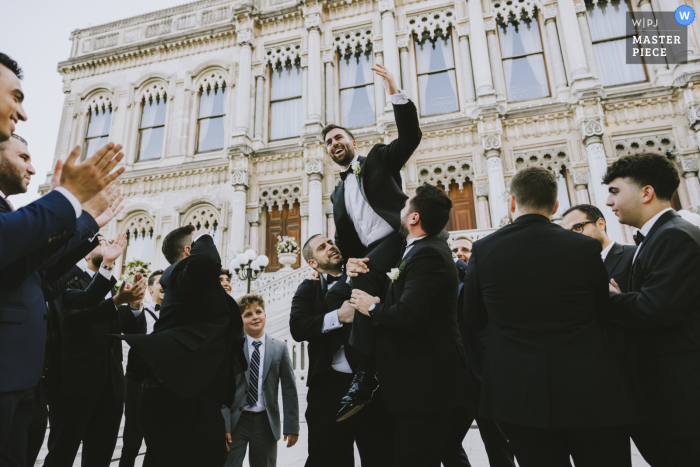 Groom Hoisted on Shoulders in Joyous Celebration at Çırağan Palace Amidst the grandeur of Çırağan Palace, the groom is hoisted high on the shoulders of his friends in a celebration and joy.