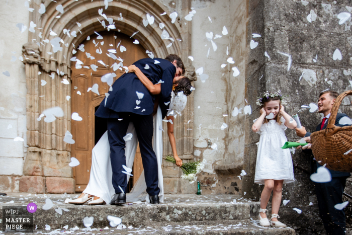 At the exit of a charming church in Île-de-France, while delicate white petals rain around the couple, a girl struggles with the loud sounds of joyous celebration.