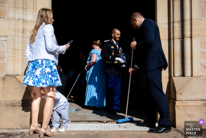 Guests Preserve Charm by Cleaning Church Exit in Île-de-France After Couple's Joyous Departure In Île-de-France, after the couple's joyous departure, guests work together to clean the exit of the old world stone-carved church, preserving its beauty and charm.