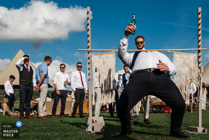 At Low Osgoodby Grange, Yorkshire, a wedding guest leans back for a limbo, creating a humorous optical illusion as if the person behind is effortlessly holding him up. 