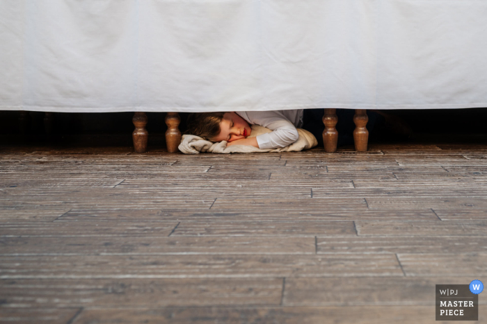 Amidst the lively celebration at the Triton Inn, Yorkshire, a young wedding guest finds a cozy refuge under a table, peacefully drifting off to sleep. 