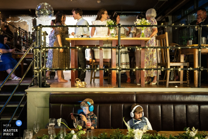 Kids Engrossed in Technology Amidst Wedding Festivities at Carpenters Mews Even the most exciting weddings can't compete with the lure of technology for these kids at Carpenters Mews. Captured by a skilled WPJA wedding photographer.