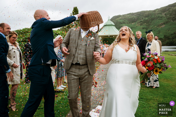 At Hotel on the Lake, the groom is showered with confetti from a dumped basket on the lush green grass outside, beautifully captured by a WPJA wedding photojournalist.