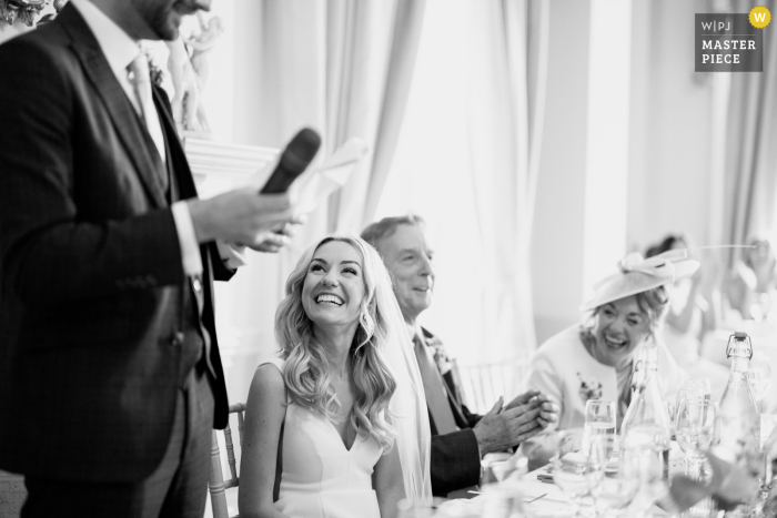 Beaming Bride Listens to Heartfelt Speech at Prestwold Hall Wedding Experience the joy and beauty captured by a WPJA wedding photojournalist at the stunning Prestwold Hall in Loughborough, UK as a beaming bride listens to a heartfelt speech.