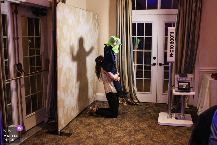 At the Riverhouse at Goodspeed Station in Haddam, Connecticut, a guest and a young child enjoy the photobooth. They have fun with hats and props, creating playful and memorable snapshots of the celebration.