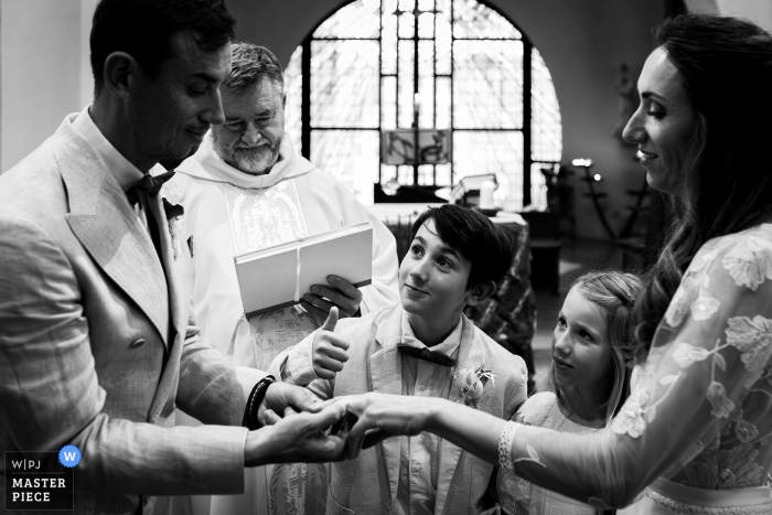 Children Gaze Lovingly at Father During Church of La Grande Motte Wedding, Celebrating Parents' Union with Joy At the Church of La Grande Motte, during the wedding celebration, a young boy and girl gaze up at father with a loving expression, reflecting happiness about parents' union. This tender moment captures the joy and familial love.