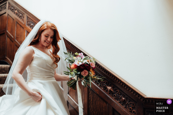 At The Walled Garden in Nottingham, UK, the bride descends the staircase with elegance and poise, creating a diagonal line across the frame. This composition accentuates her graceful entrance and adds visual interest to the moment.