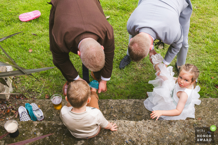 Wicklow Wedding: Adults, Children Aid Shoe Recovery on Grass At a reception venue in County Wicklow, Leinster, adults help children put their shoes back on while outside on the grass during the wedding reception.