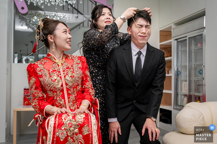 At the bride's home in Yilan County, Taiwan, a humorous moment unfolds as the groom's face gets stuck in a puzzled expression while his mother-in-law attempts to put a gold necklace on him. This lighthearted scene adds a touch of levity to the wedding.