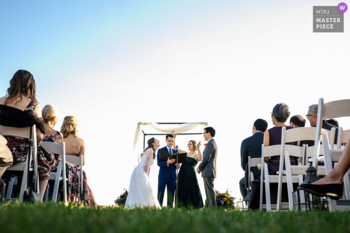 Joyful Exchange Highlights Ceremony at the Inn at Long Shore At the Inn at Long Shore in Westport, CT, the couple shares a laugh during their outdoor ceremony on the grass. The bride exudes joy and connection at this special moment.