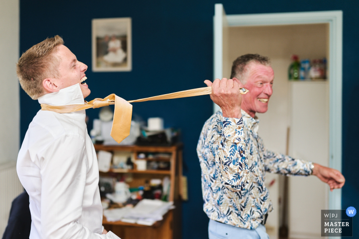 Father of the groom playfully drags his son by the tie at Amsterdam Noord Holland home, capturing a humorous moment.