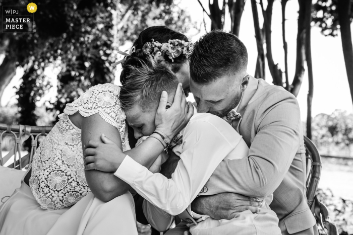 In Mauguio, France, the photographer artistically captures the bride and groom hugging their son in a tight black-and-white embrace outdoors, beautifully conveying heartfelt family love and emotional depth.